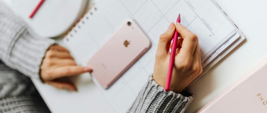 Picture of a woman scheduling her workweek with a phone and a notebook.