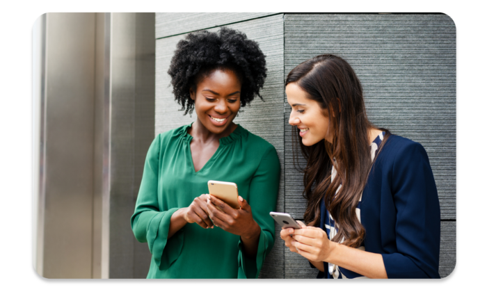 Two women smiling while one shows the other something on her phone.